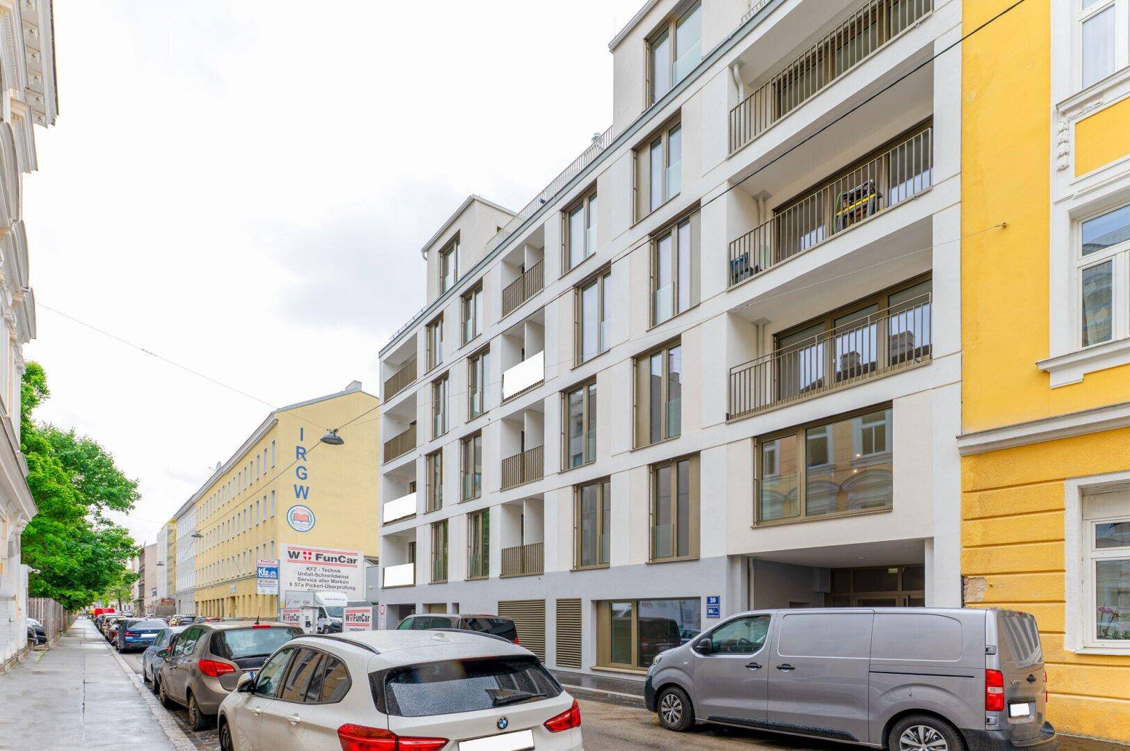 Moderne Wohnhausfassade mit Balkonen und großen Fenstern in einer städtischen Umgebung.