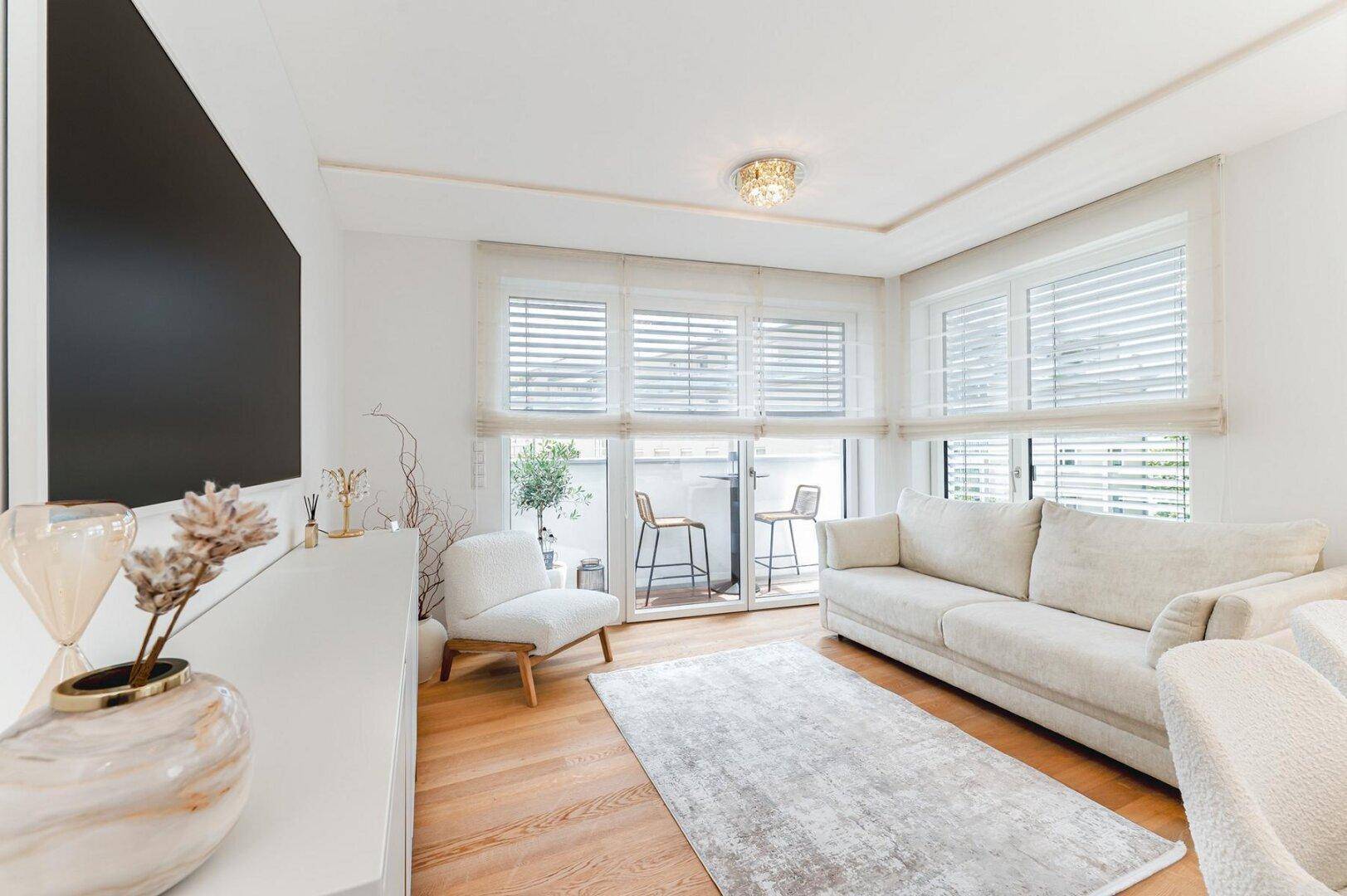 Helles Wohnzimmer mit beigem Sofa, Holzboden und Zugang zum Balkon durch große Fenster.