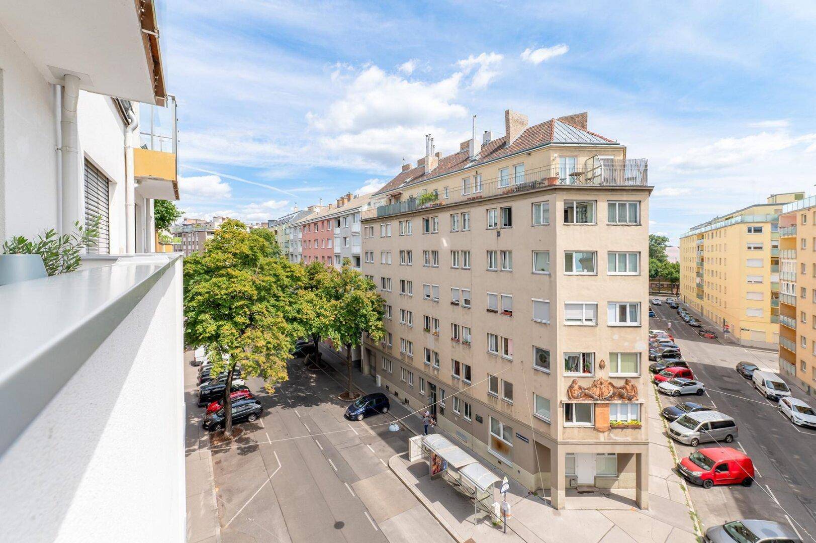 Balkon mit Blick auf die Straße und die umliegenden Wohngebäude unter blauem Himmel.