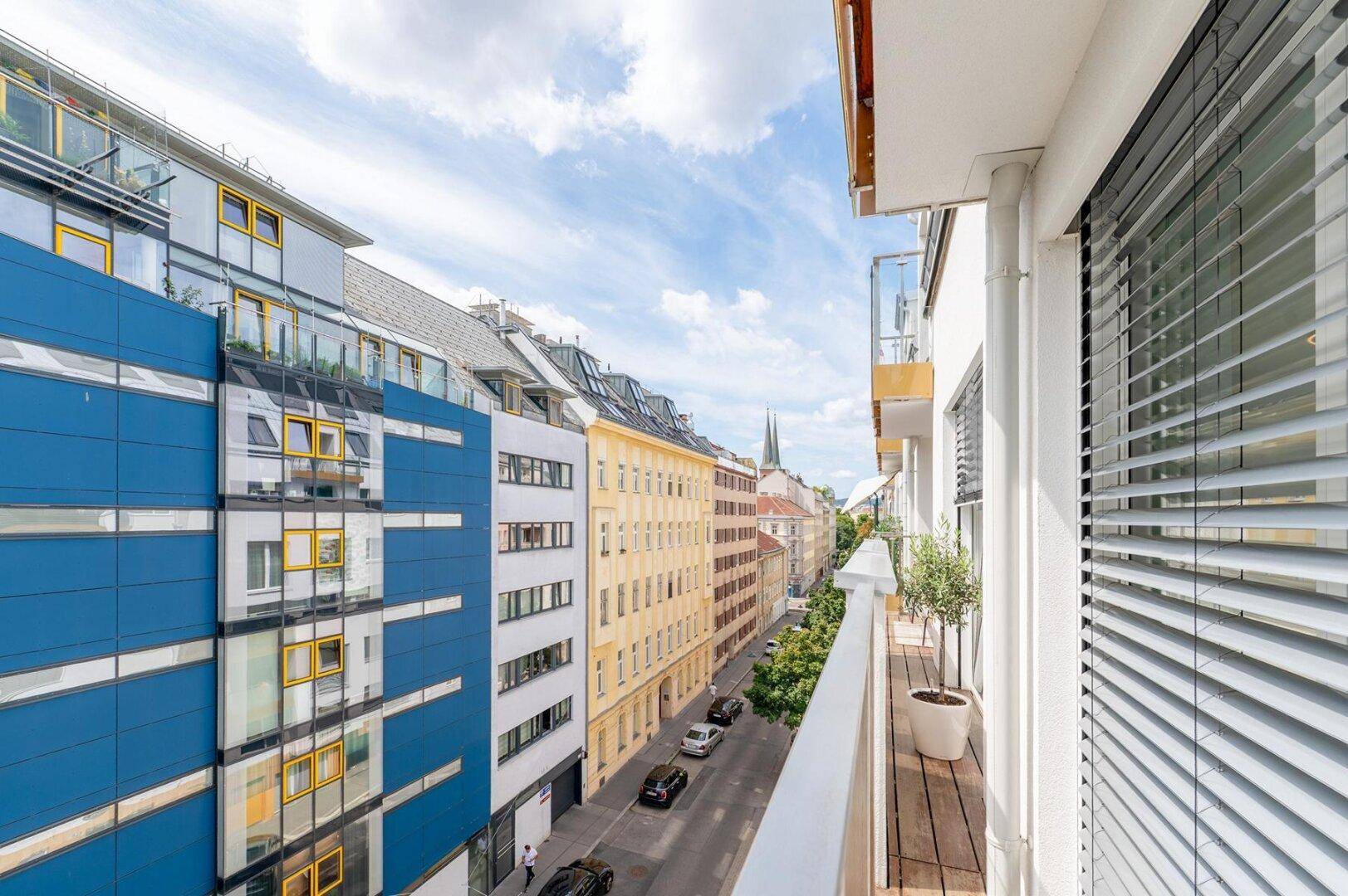 Schmaler Balkon mit Holzboden und Blick auf die belebte Straße und moderne Gebäude.