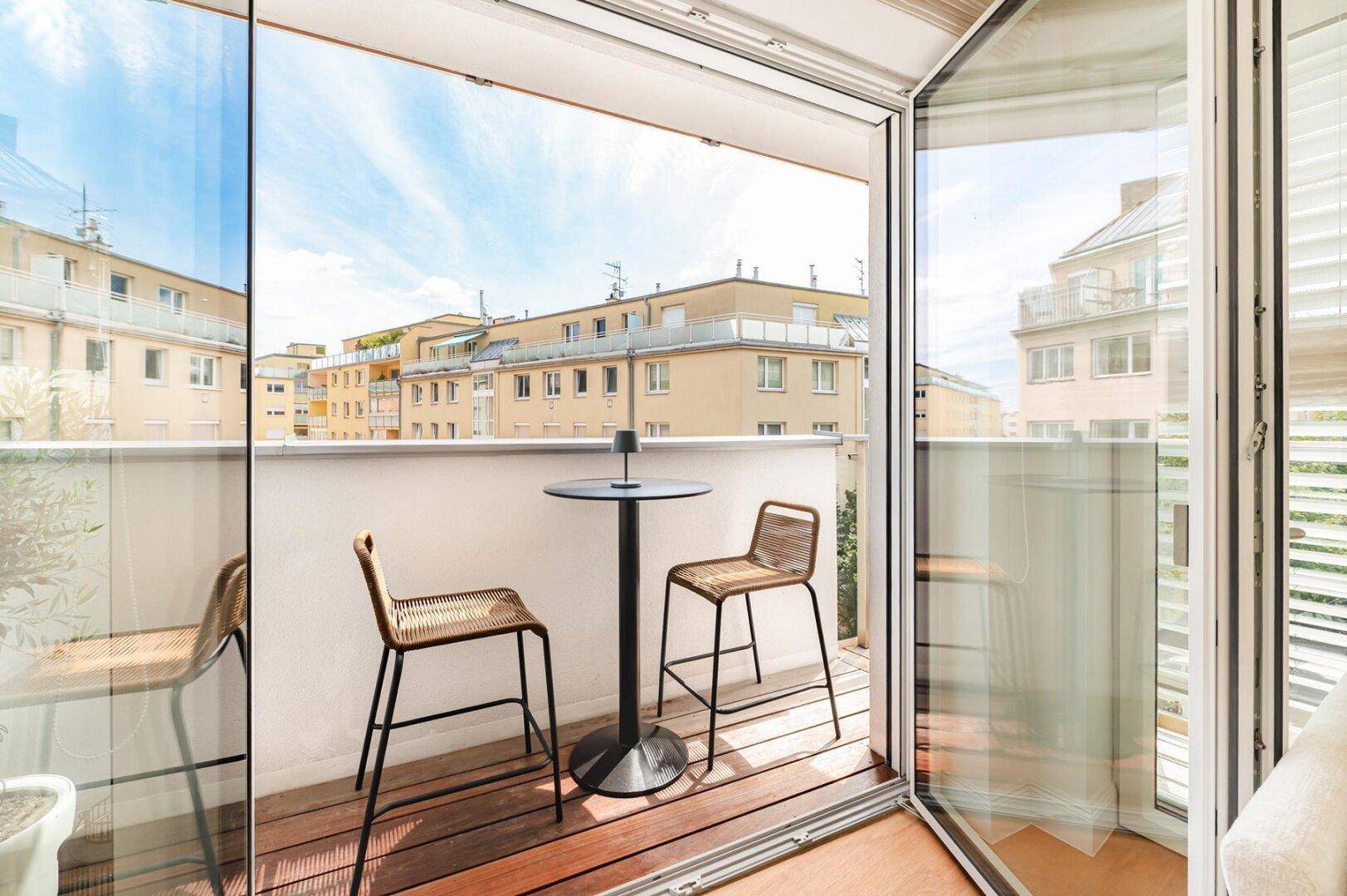 Heller Balkon mit Glasfront und Sitzgelegenheiten, bietet einen weiten Blick über die Stadt.