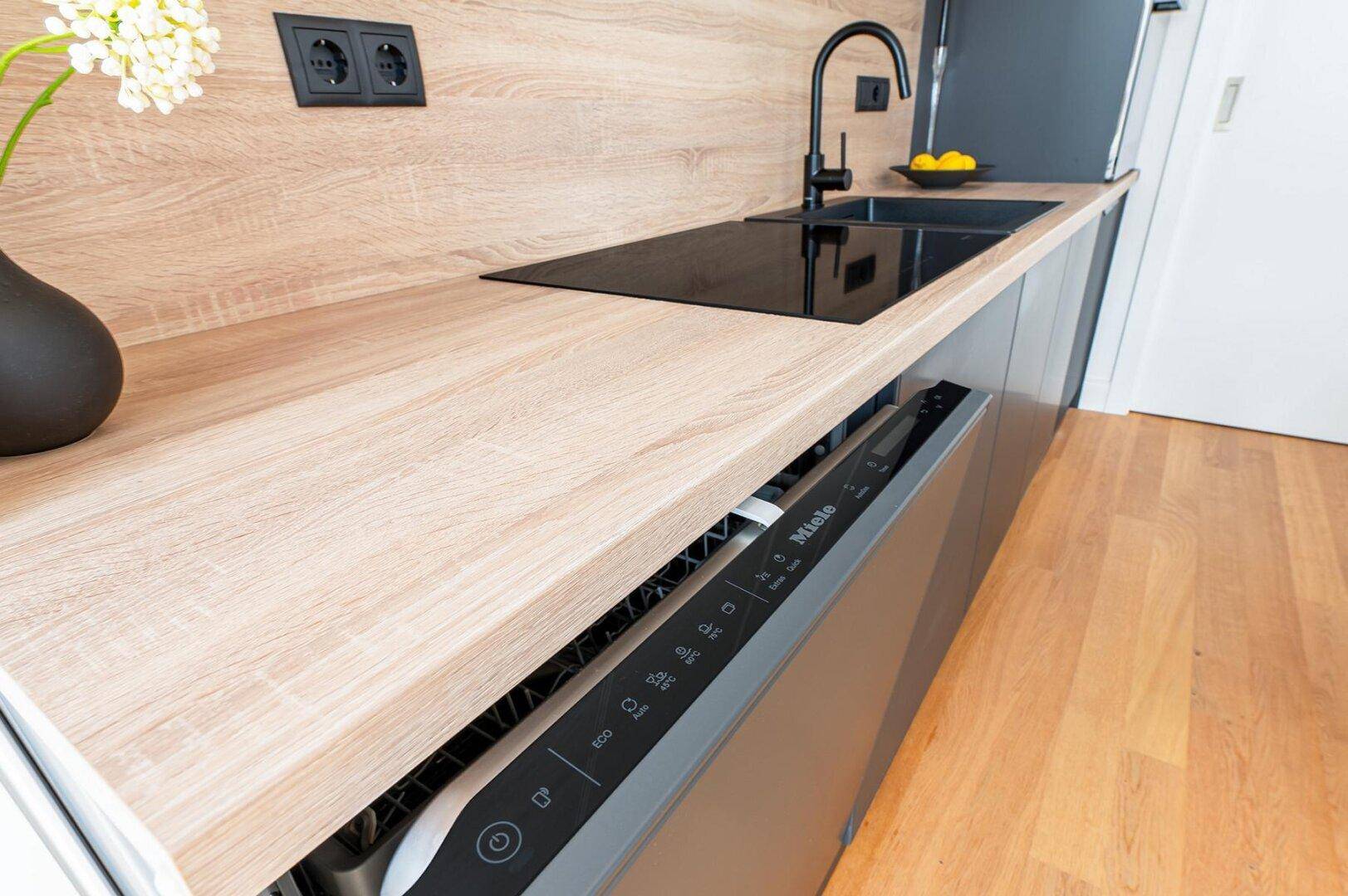 Integrierter Geschirrspüler in der modernen Küche mit Holz-Arbeitsplatte und Holzboden.