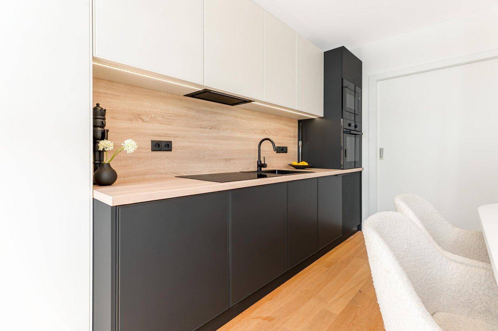 Detailansicht der modernen Küche mit Holz-Arbeitsplatte, Induktionskochfeld und schwarzer Spüle.