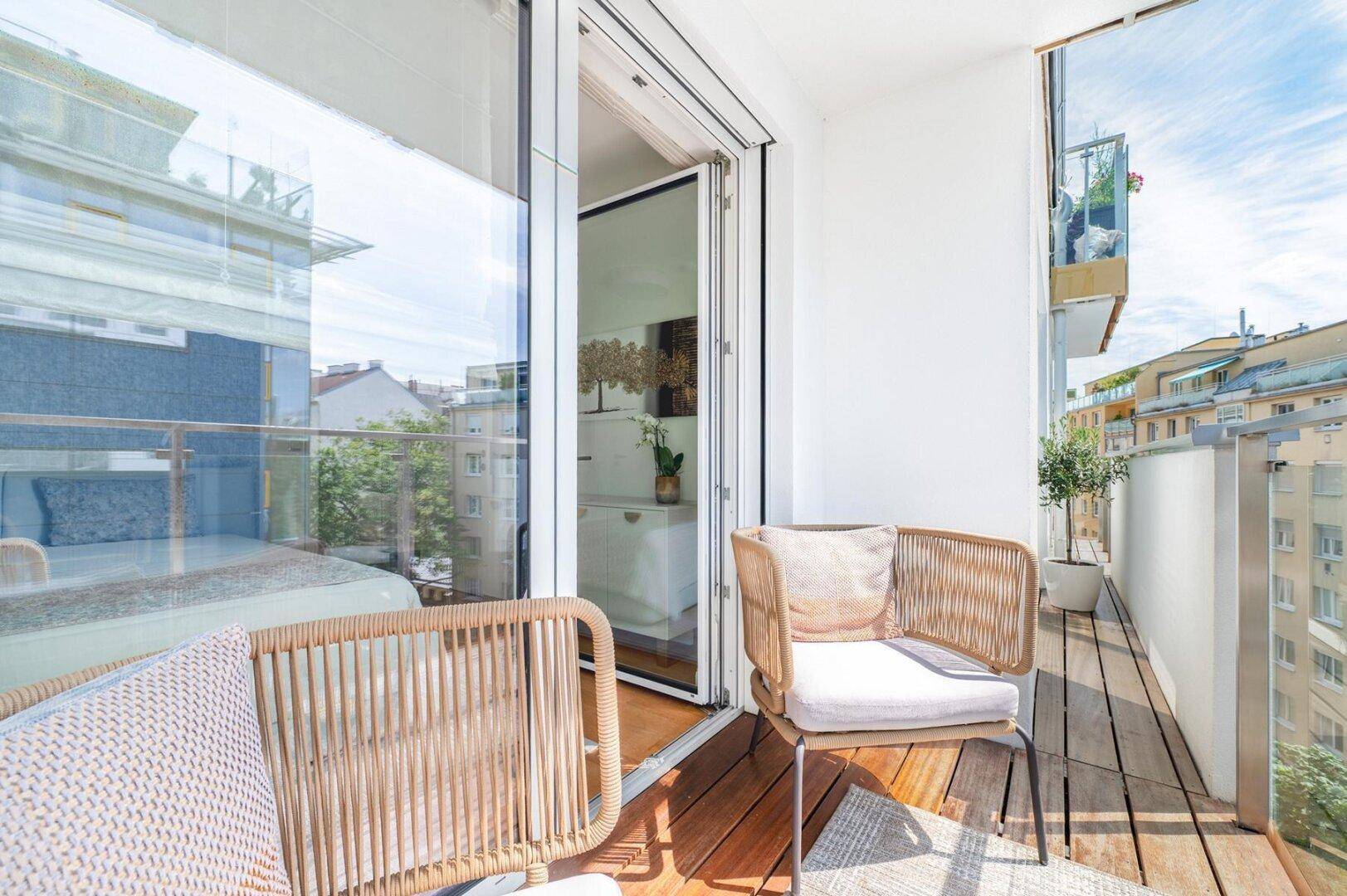 Heller Balkon mit Holzboden und bequemen Sitzgelegenheiten, mit Blick auf die Stadt.