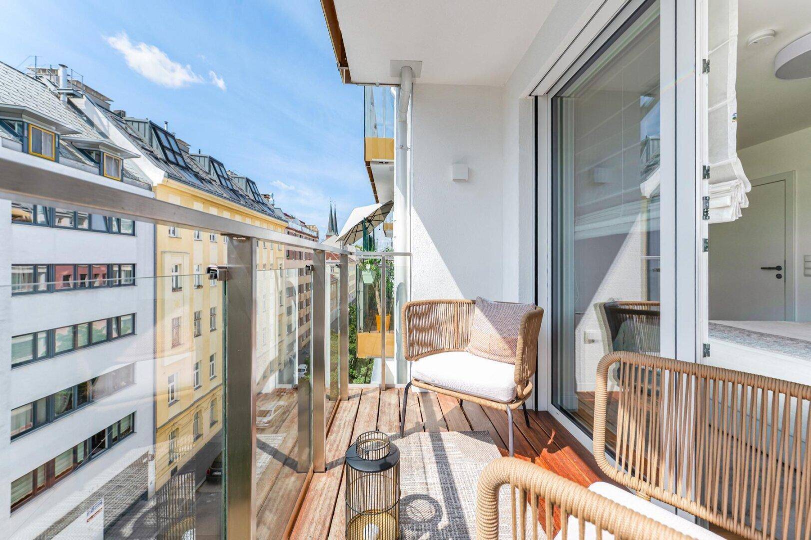 Schmaler Balkon mit Glasgeländer und Holzboden, bietet einen weiten Blick über die Straße.