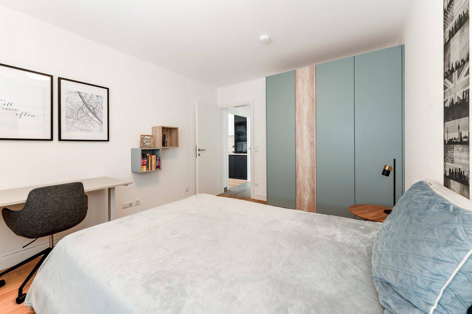 Schlafzimmer mit Einzelbett, Schreibtisch und farbigen Einbauschränken, bietet viel Stauraum.