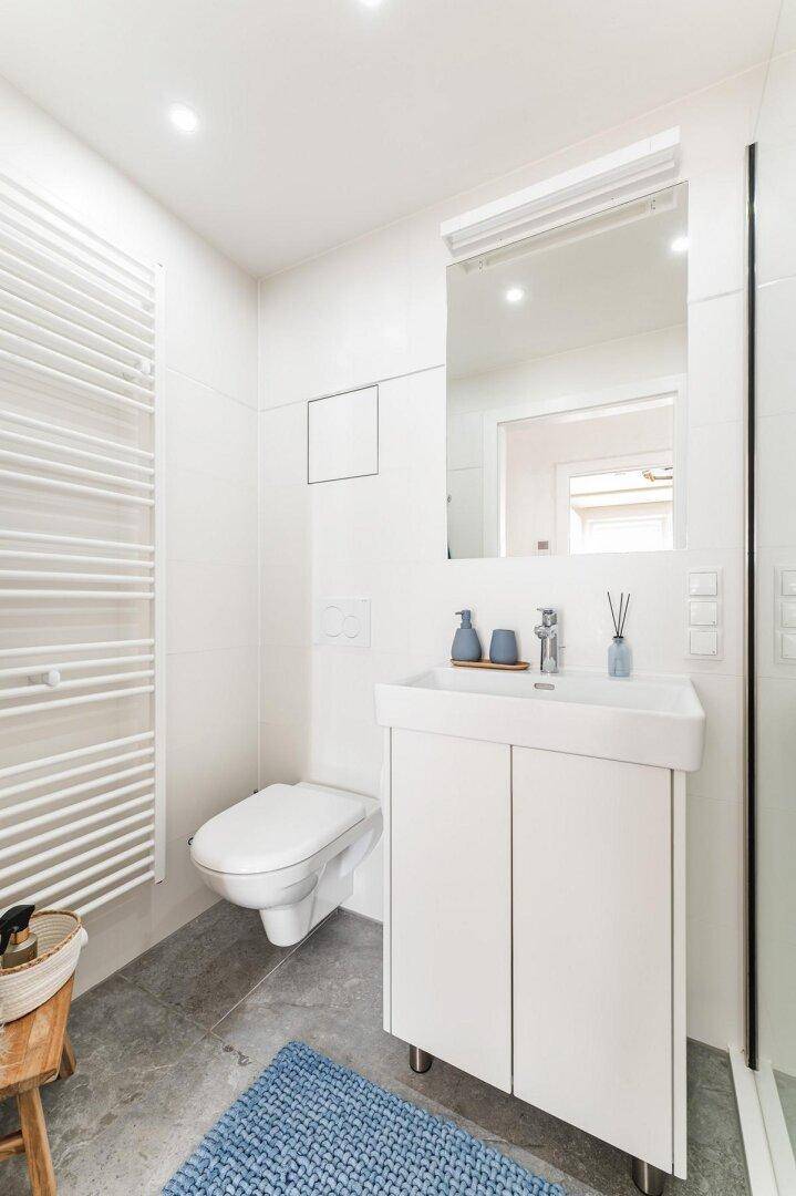 Helles Badezimmer mit wandhängendem WC, Waschtisch und beheiztem Handtuchhalter.