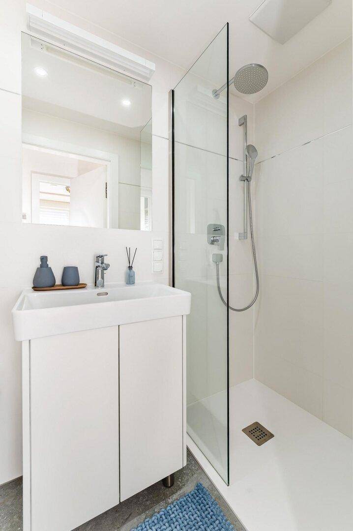 Modernes Badezimmer mit weißem Waschtischunterschrank, Spiegel und begehbarer Dusche.