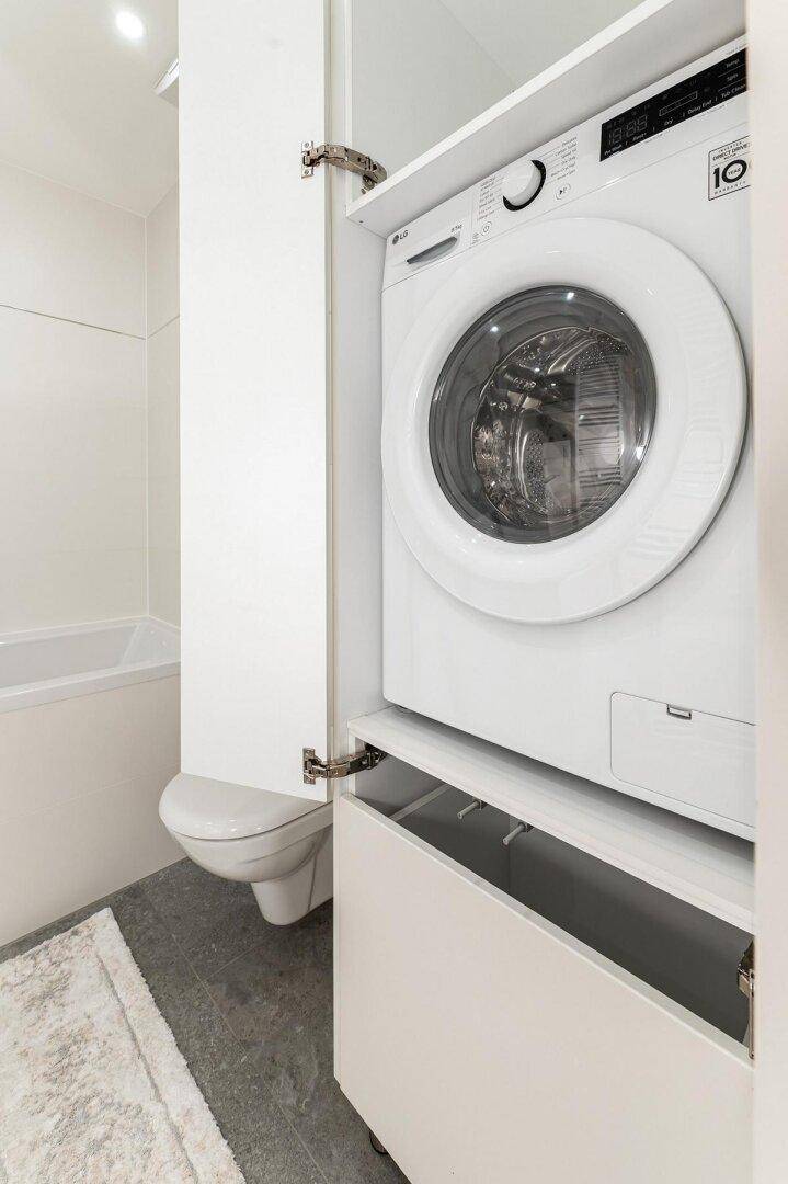 Badezimmer mit integrierter Waschmaschine, Badewanne und modernen Fliesen.