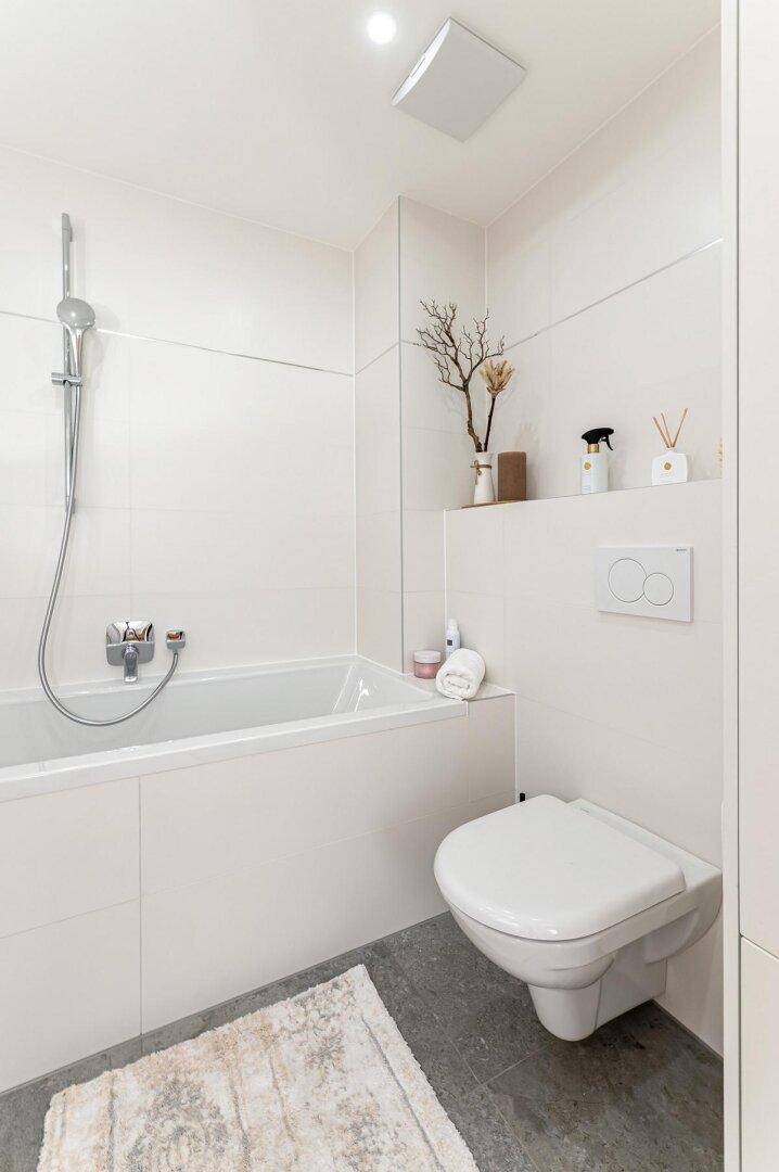 Helles Badezimmer mit wandhängendem WC, Badewanne und modernen Fliesen.