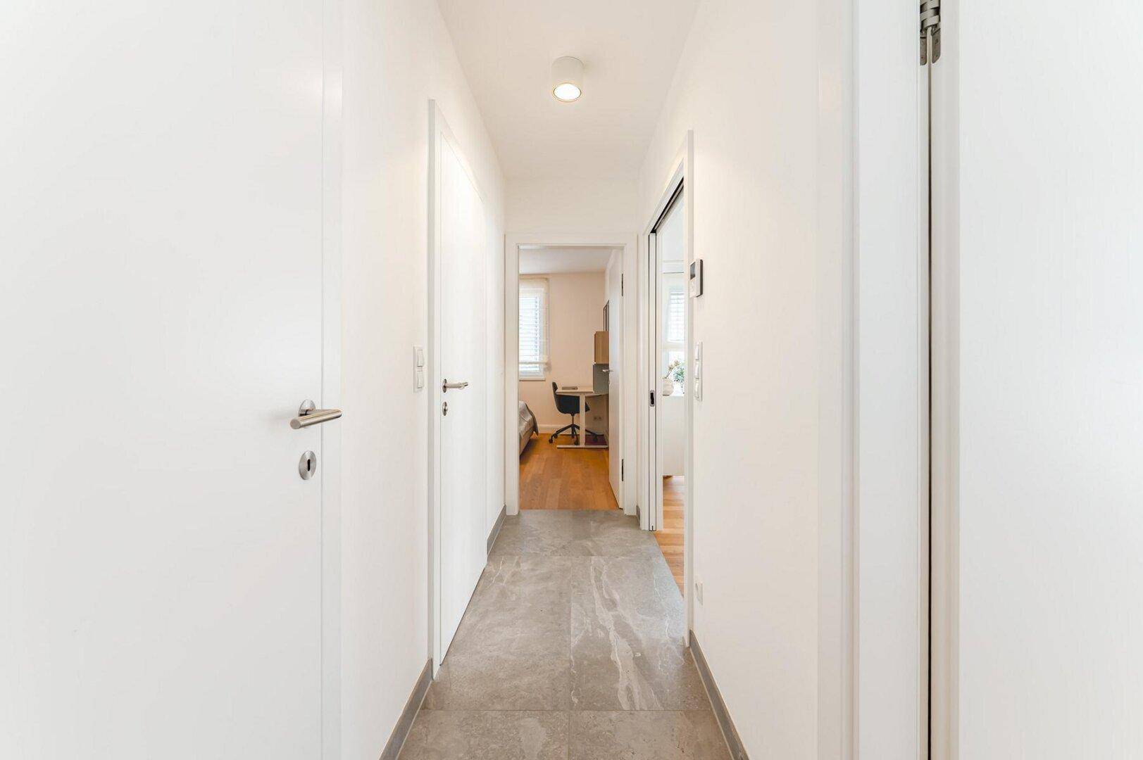 Heller Flur mit Fliesenboden, weißen Türen und Blick in angrenzende Zimmer.