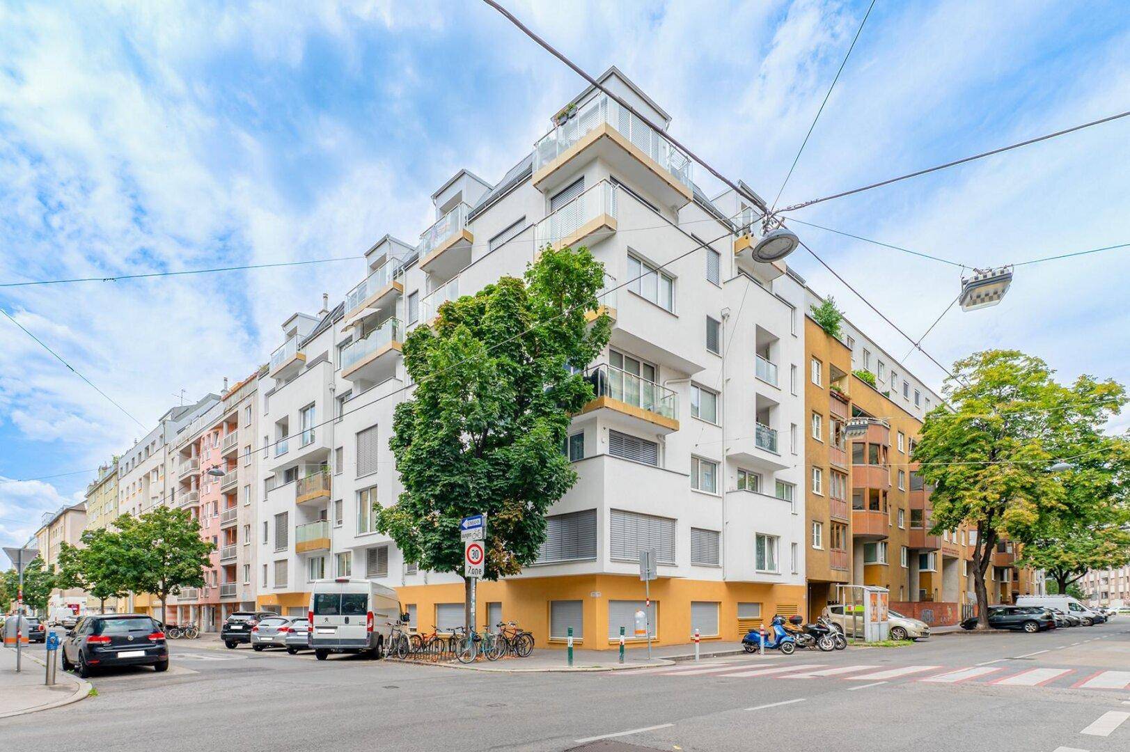 Modernes Eckgebäude mit Balkonen und großen Fenstern an einer belebten Straße.