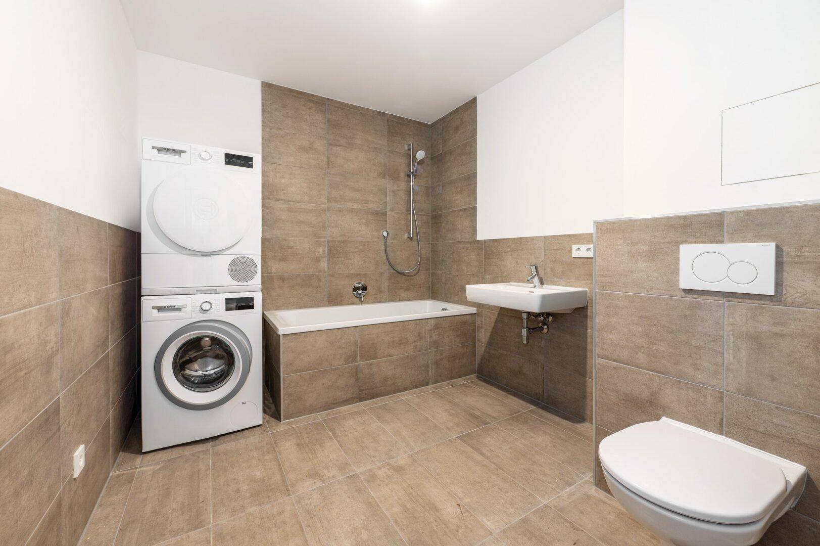 Modernes Badezimmer mit Badewanne, Dusche, wandhängendem WC, Waschbecken und integrierter Waschmaschine sowie Trockner.