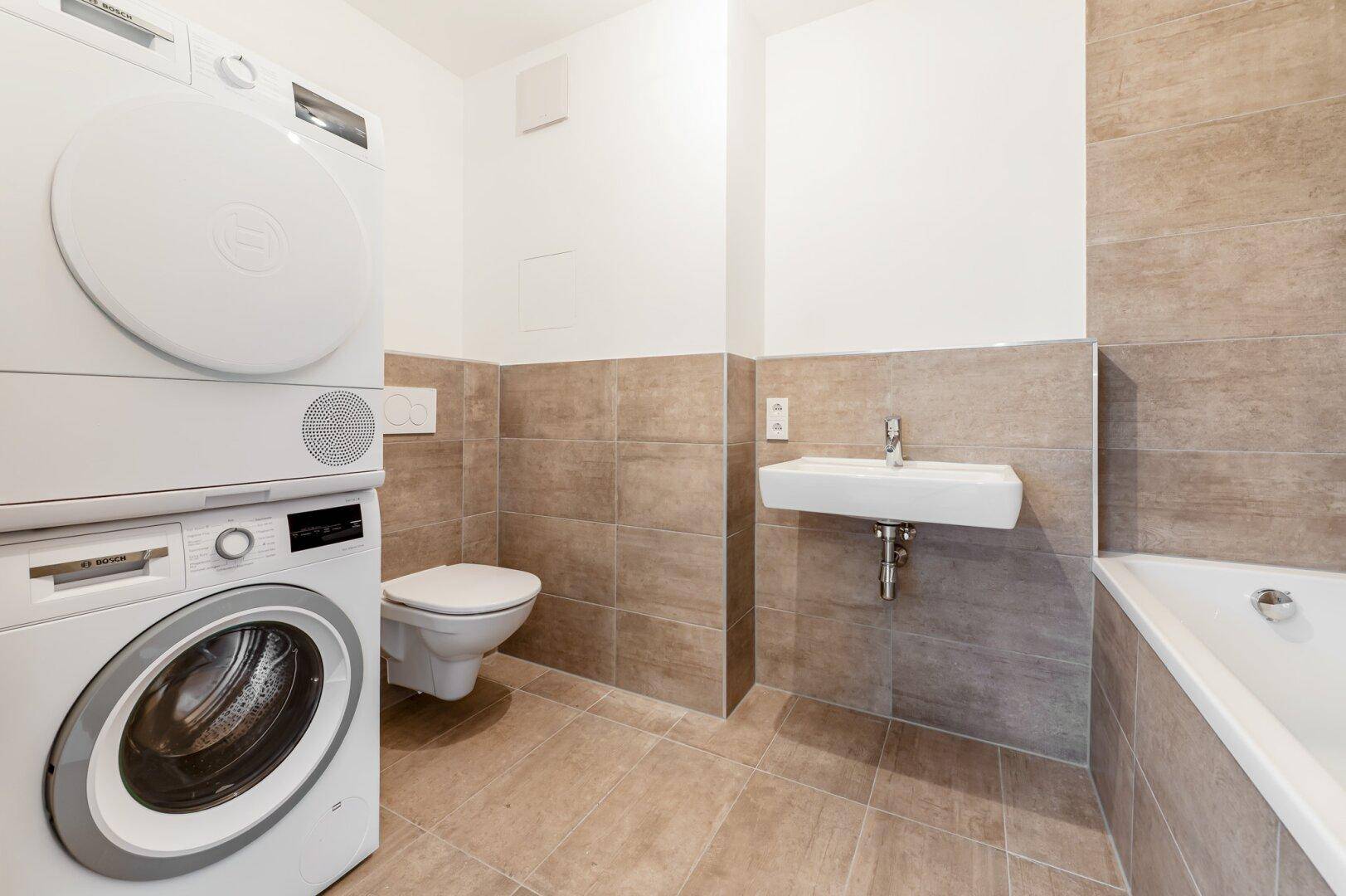 Helles Badezimmer mit Waschmaschine, Trockner, Badewanne, WC und modernem Waschbecken.