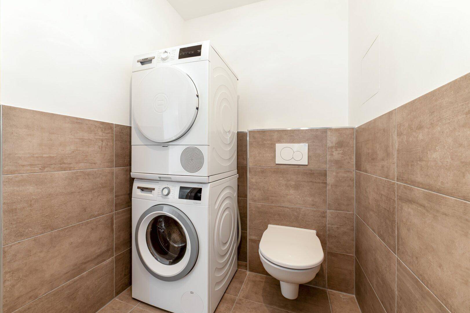 Funktionales Badezimmer mit gestapelter Waschmaschine und Trockner neben der Toilette.
