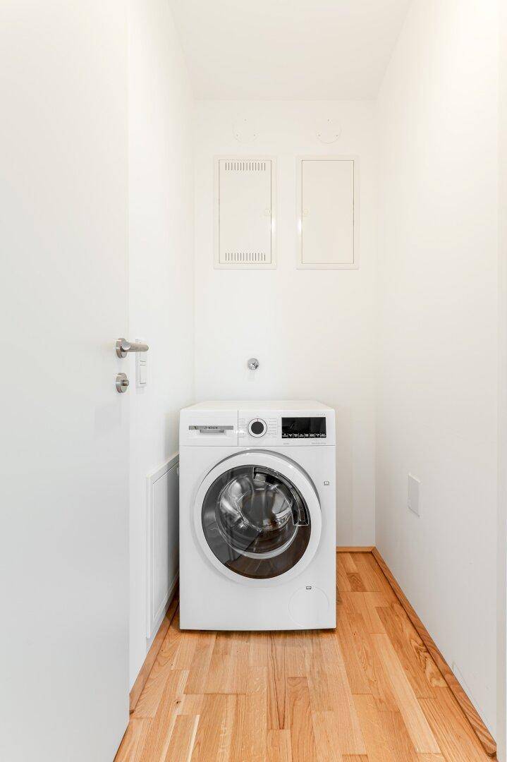 Heller Hauswirtschaftsraum mit Waschmaschine und Holzboden.