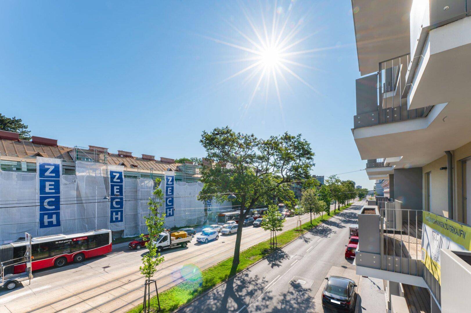 Sonniger Blick von einem Balkon auf die belebte Straße mit Trambahnschienen und umliegenden Gebäuden.