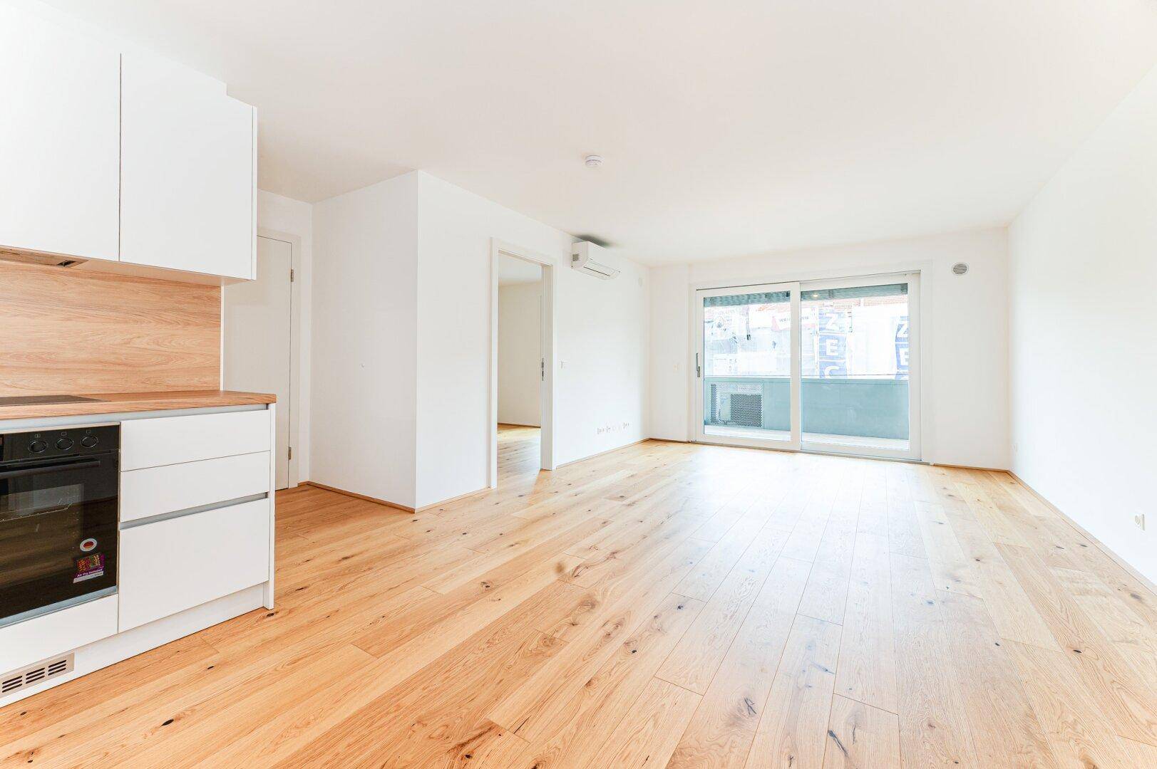 Heller Wohnbereich mit Holzboden und Zugang zu einem Balkon, bereit für die individuelle Gestaltung.