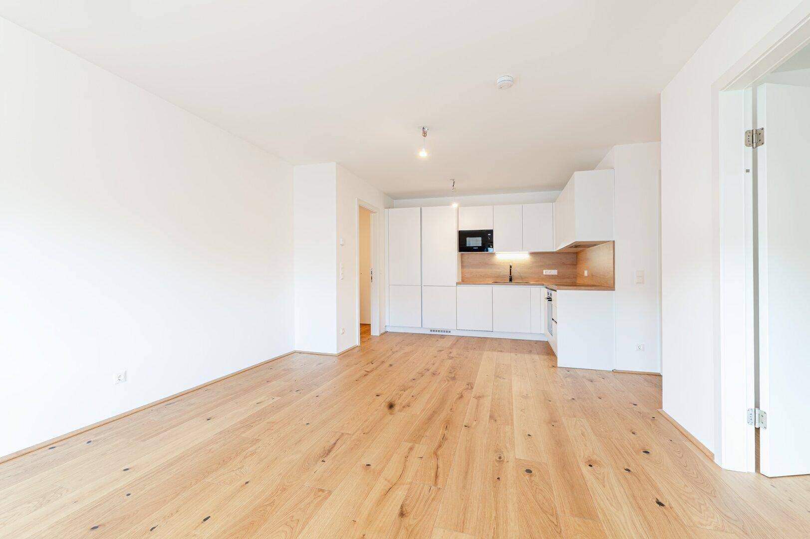 Geräumiger, heller Wohnbereich mit offener Küche und hochwertigem Holzboden, ideal für modernes Wohnen.