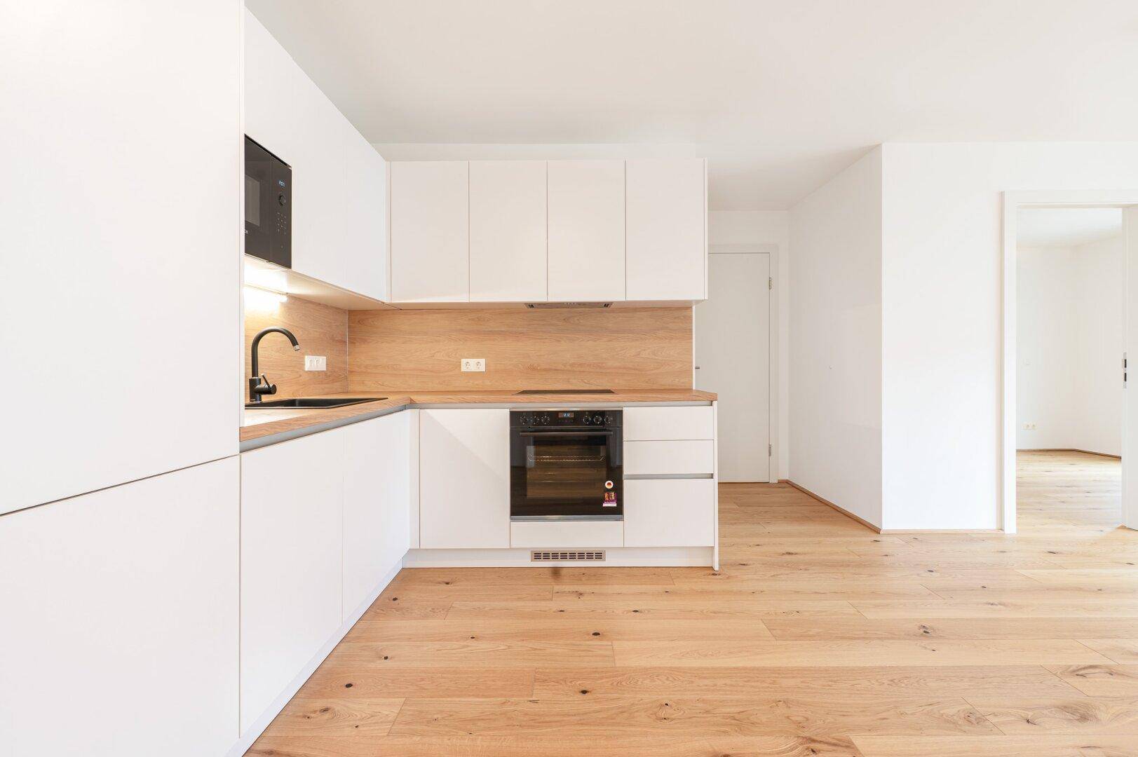 Stilvolle, weiße Einbauküche mit Holzdetails und modernen Geräten, bereit zum Kochen und Genießen.