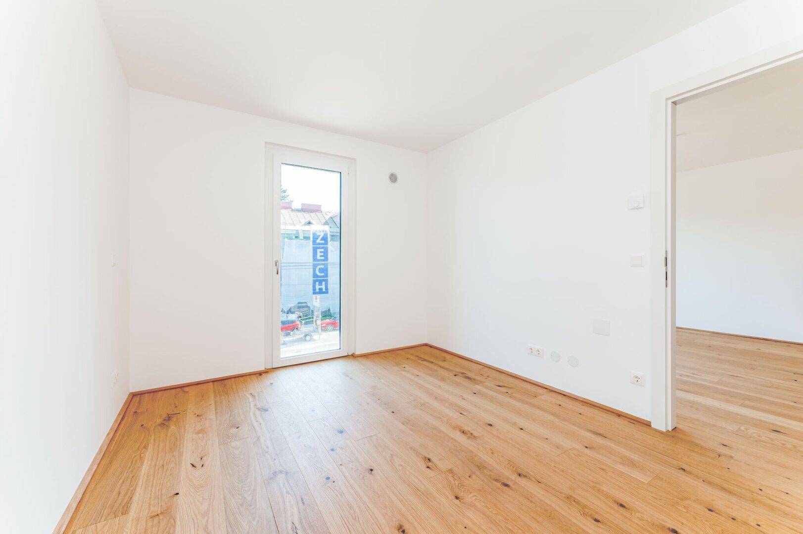 Helles Zimmer mit Holzboden und großem Fenster, das viel Tageslicht hereinlässt.