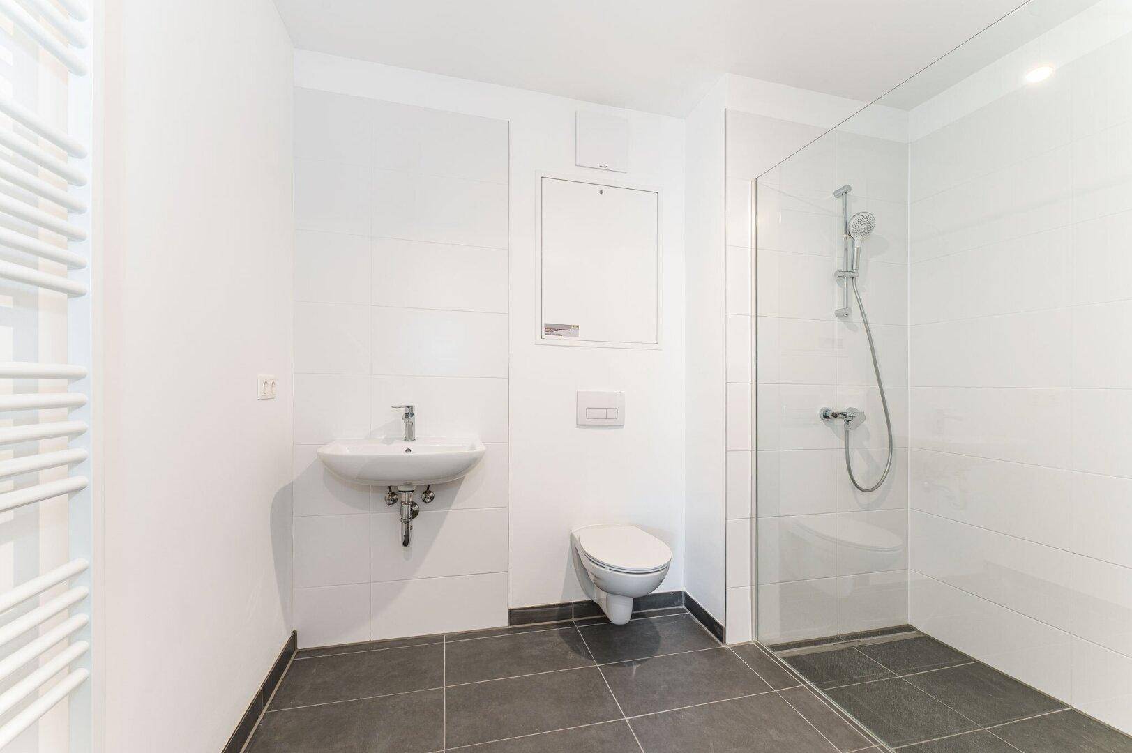 Modernes Badezimmer mit Dusche, Wand-WC und beheiztem Handtuchhalter in neutralen Farben.