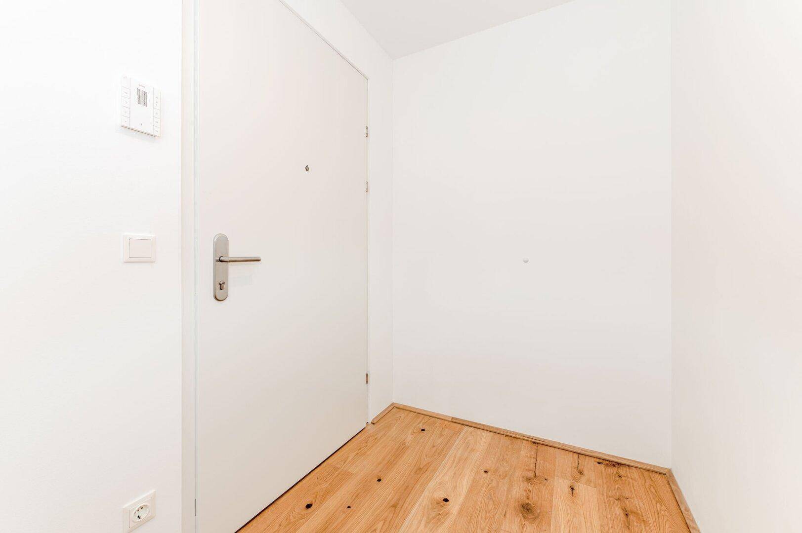 Eingangsbereich mit weißer Tür und Holzboden, der einen sauberen und modernen Eindruck vermittelt.