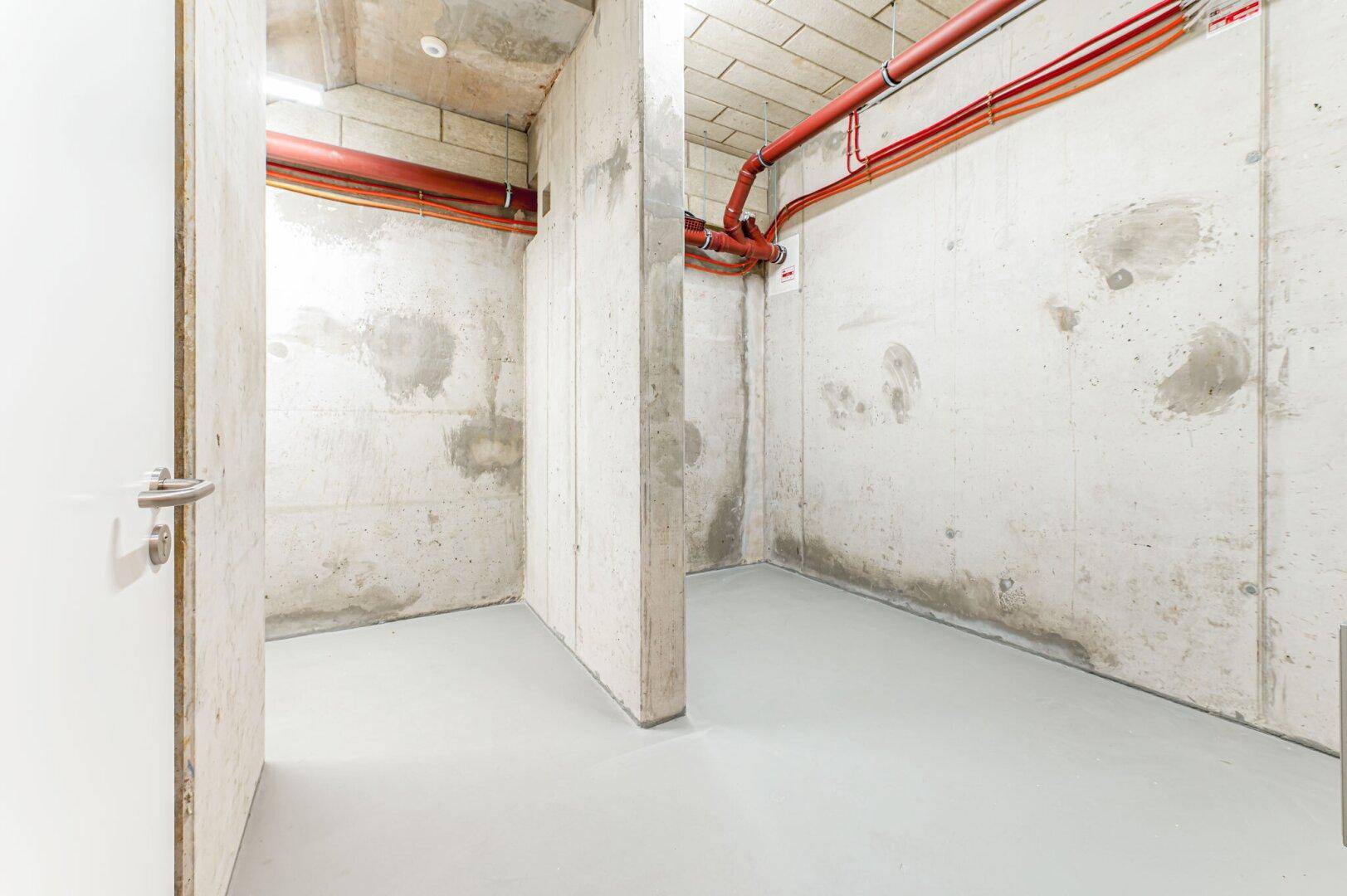 Unausgebauter Kellerraum mit Betonwänden und sichtbaren Leitungen, ideal als Lagerfläche.