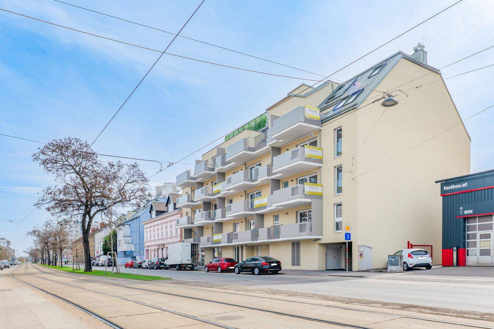 Moderne Wohnanlage mit mehreren Balkonen und einer hellen Fassade entlang einer Straße.