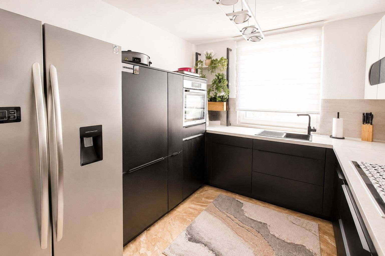 Moderne Küche mit schwarzen Unterschränken, hellem Arbeitsbereich und großem Kühlschrank.