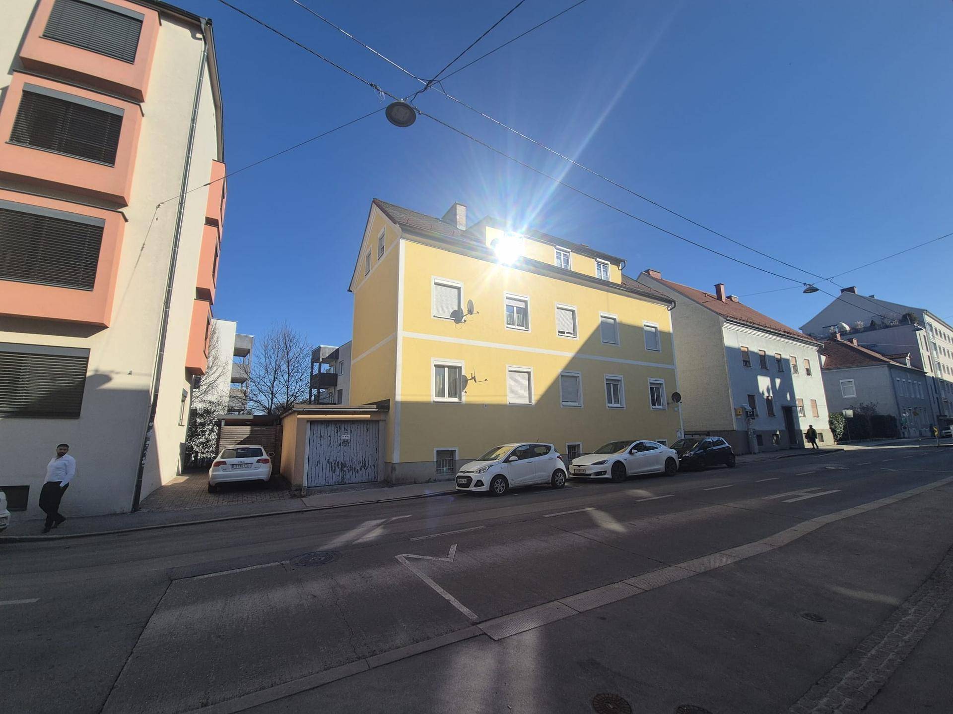 Gelbes Mehrfamilienhaus an einem sonnigen Tag von der Straße aus gesehen.