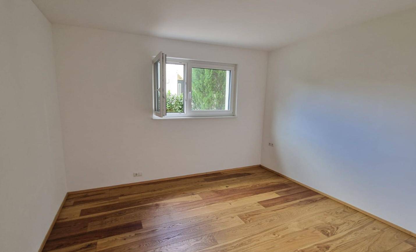 Ruhiges Schlafzimmer mit Holzboden und Fenster, das viel Tageslicht hereinlässt.
