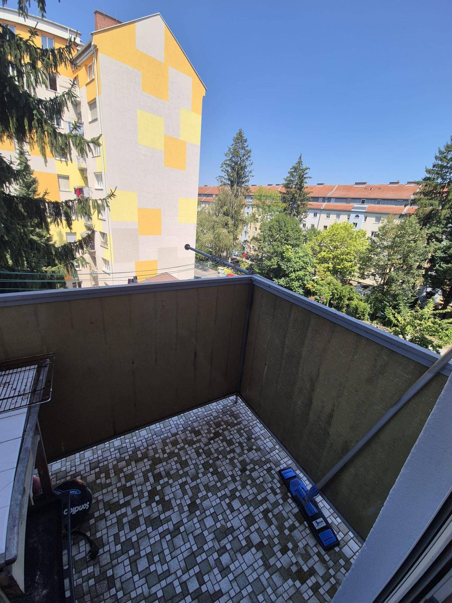 Leerer Balkon mit Fliesenboden und weitem Blick über die Nachbarschaft.