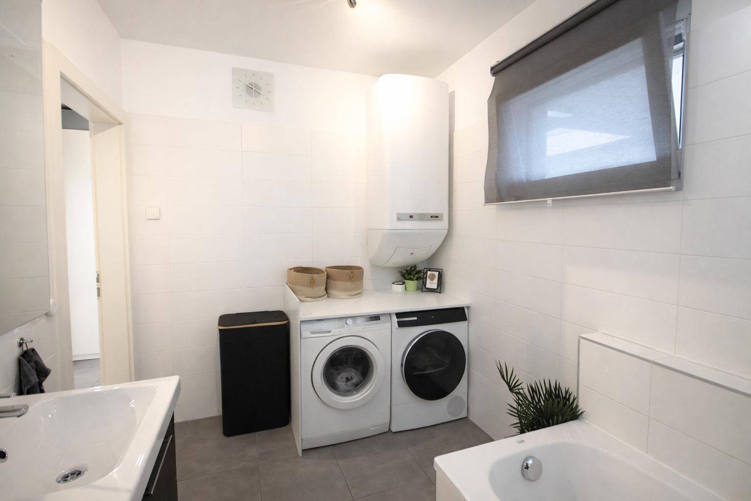 Badezimmer mit Badewanne, Waschmaschine, Trockner und Fenster für natürliche Belüftung.