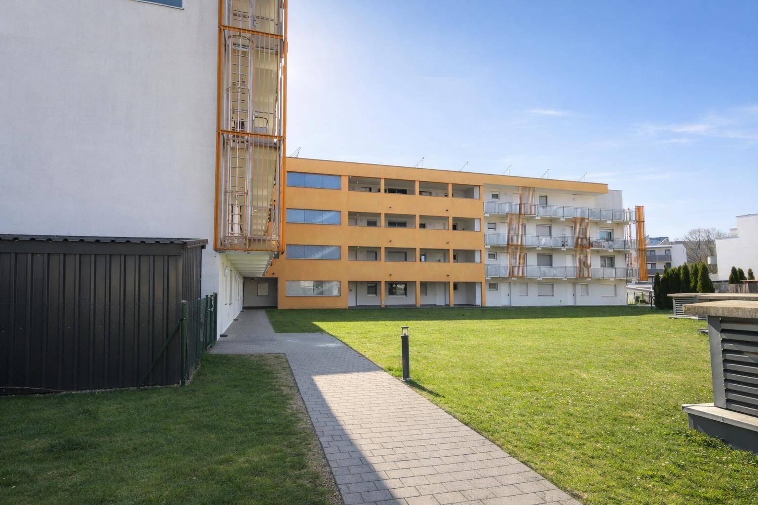 Moderne Wohnanlage mit gepflegter Grünfläche und Gehwegen unter strahlendem Himmel.