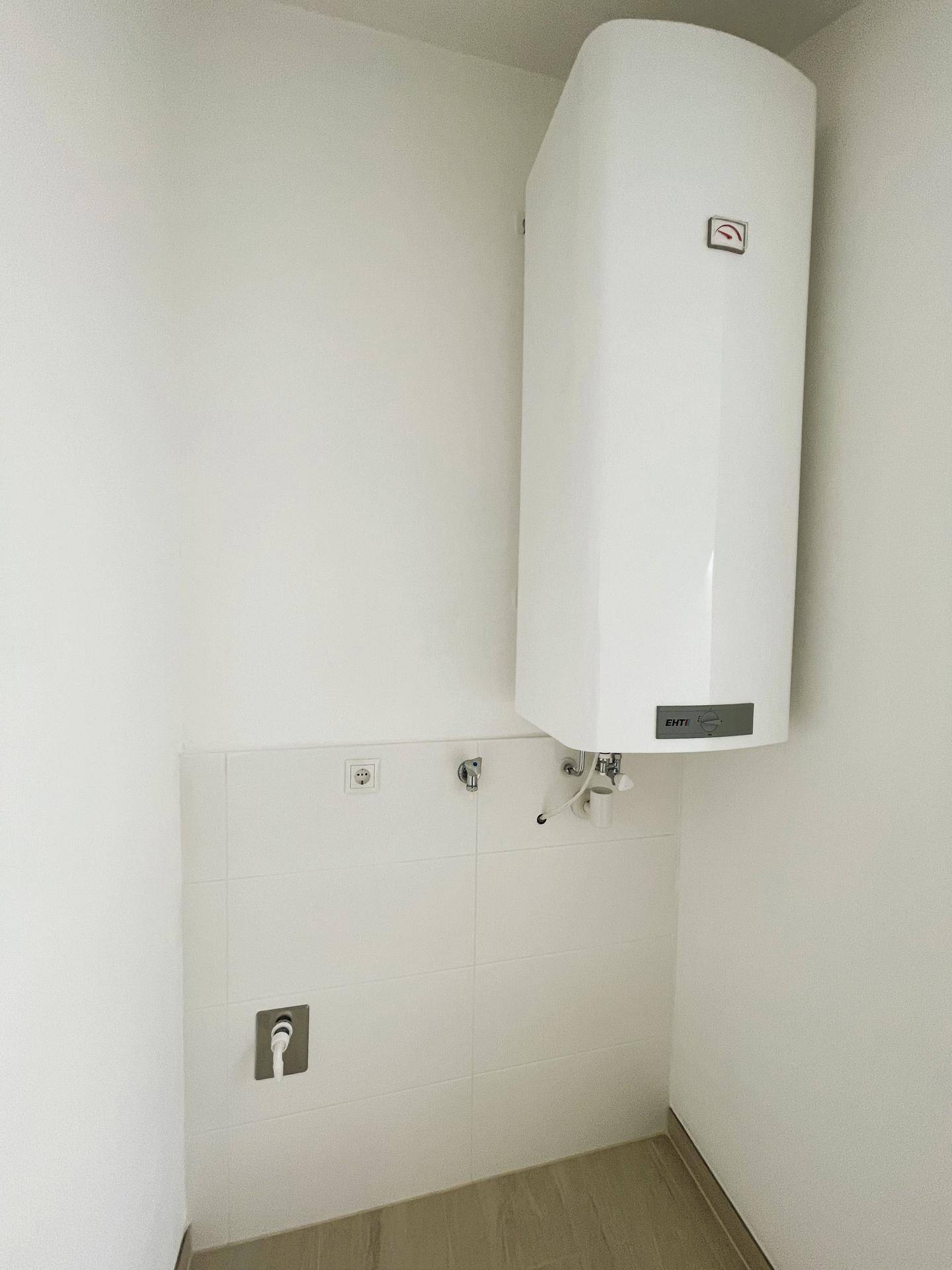 Praktischer Hauswirtschaftsraum mit Warmwasserboiler und Anschlüssen für Waschmaschine.