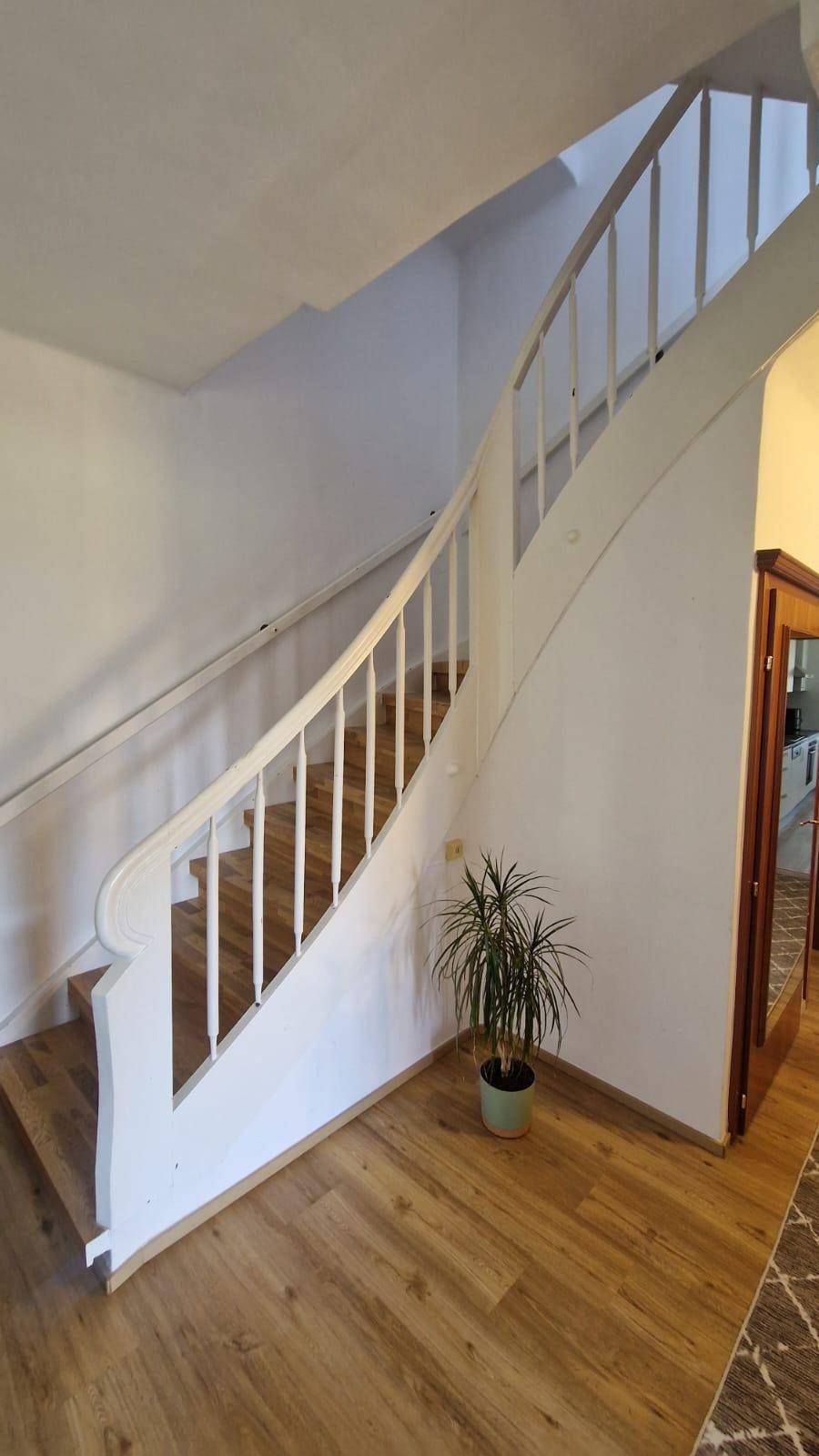 Elegante Holztreppe im Flur mit weißem Geländer, die die Etagen des Hauses verbindet.