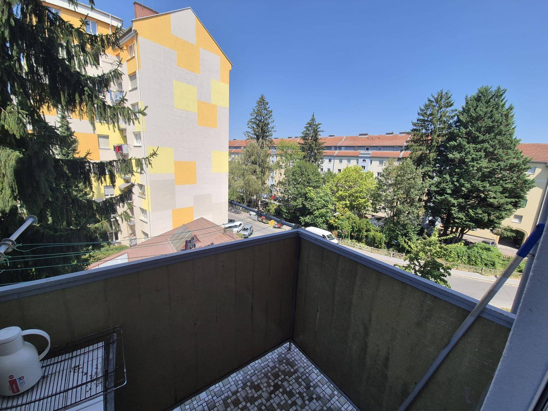 Blick vom Balkon auf grüne Bäume und die umliegende Wohnbebauung.