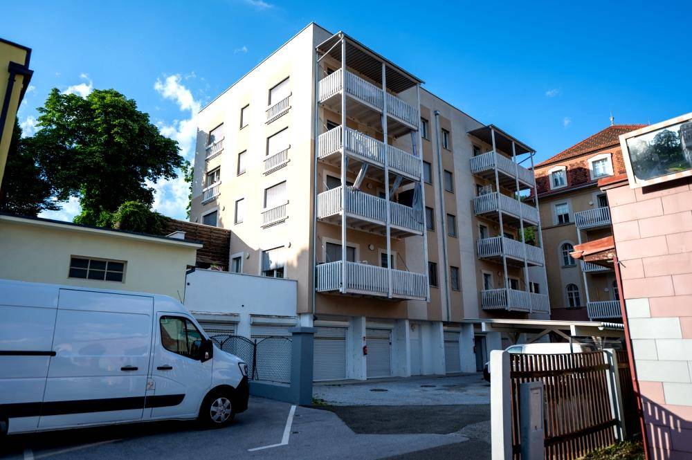Modernes Wohngebäude mit Balkonen, Garagen und einem Lieferwagen auf dem Parkplatz.