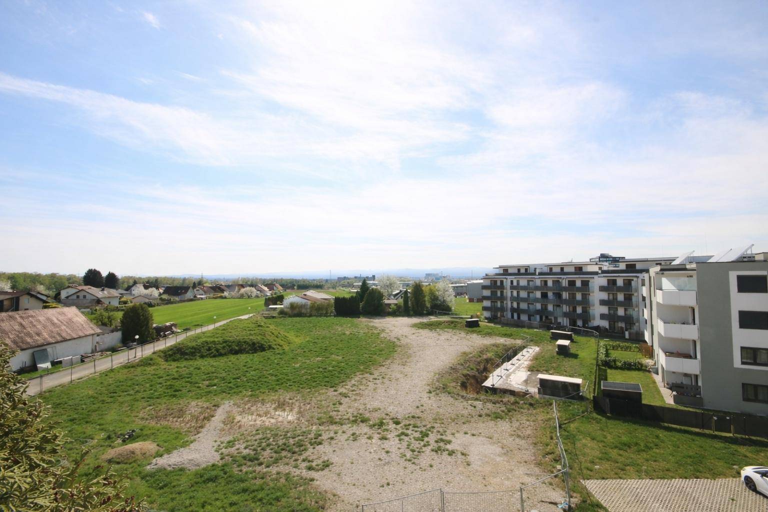 Weitläufiger Blick über grüne Felder und die umliegende Wohnbebauung unter blauem Himmel.