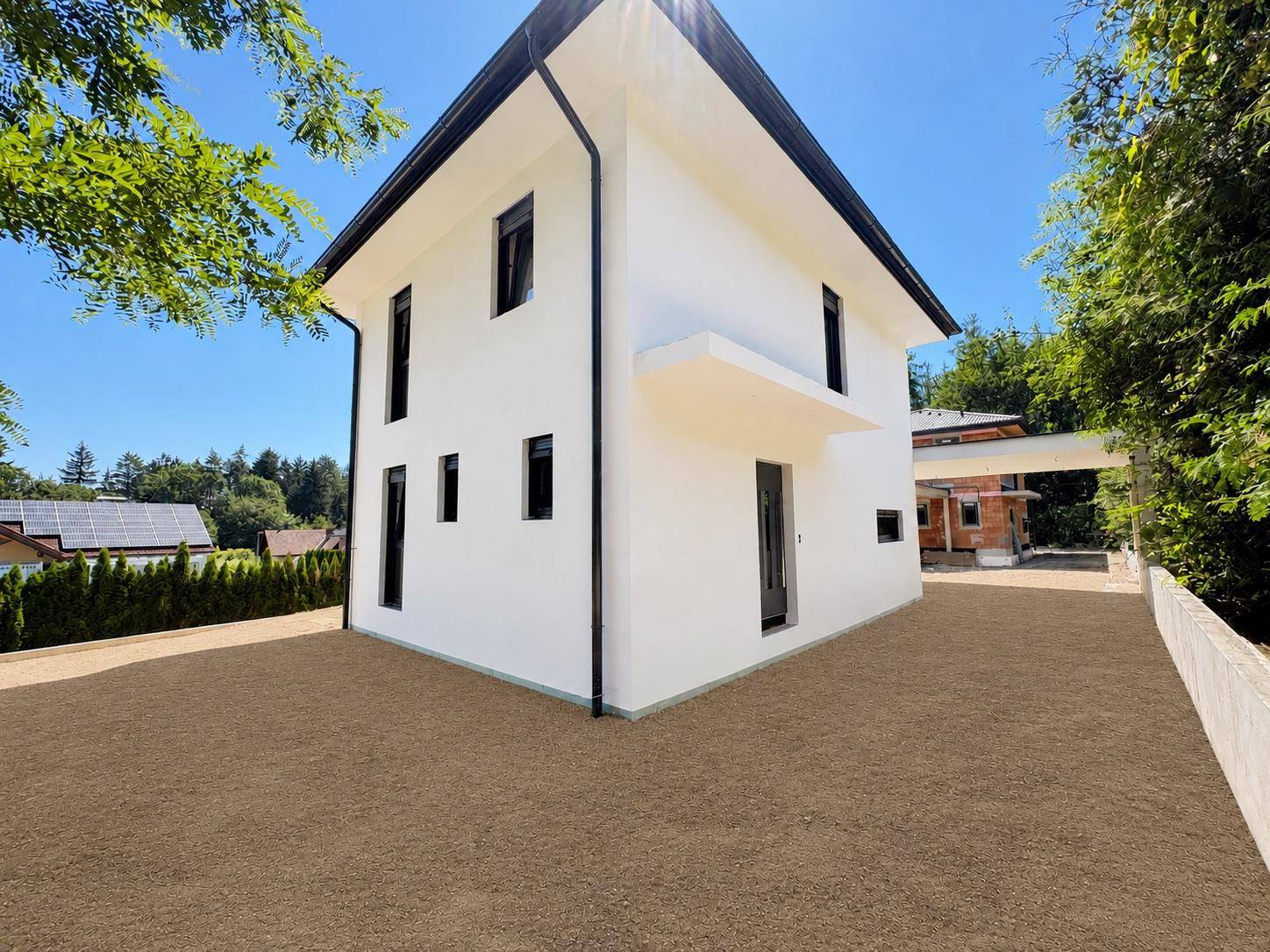 Schräge Außenansicht des modernen Hauses mit mehreren Fenstern und weitläufiger Kiesfläche.