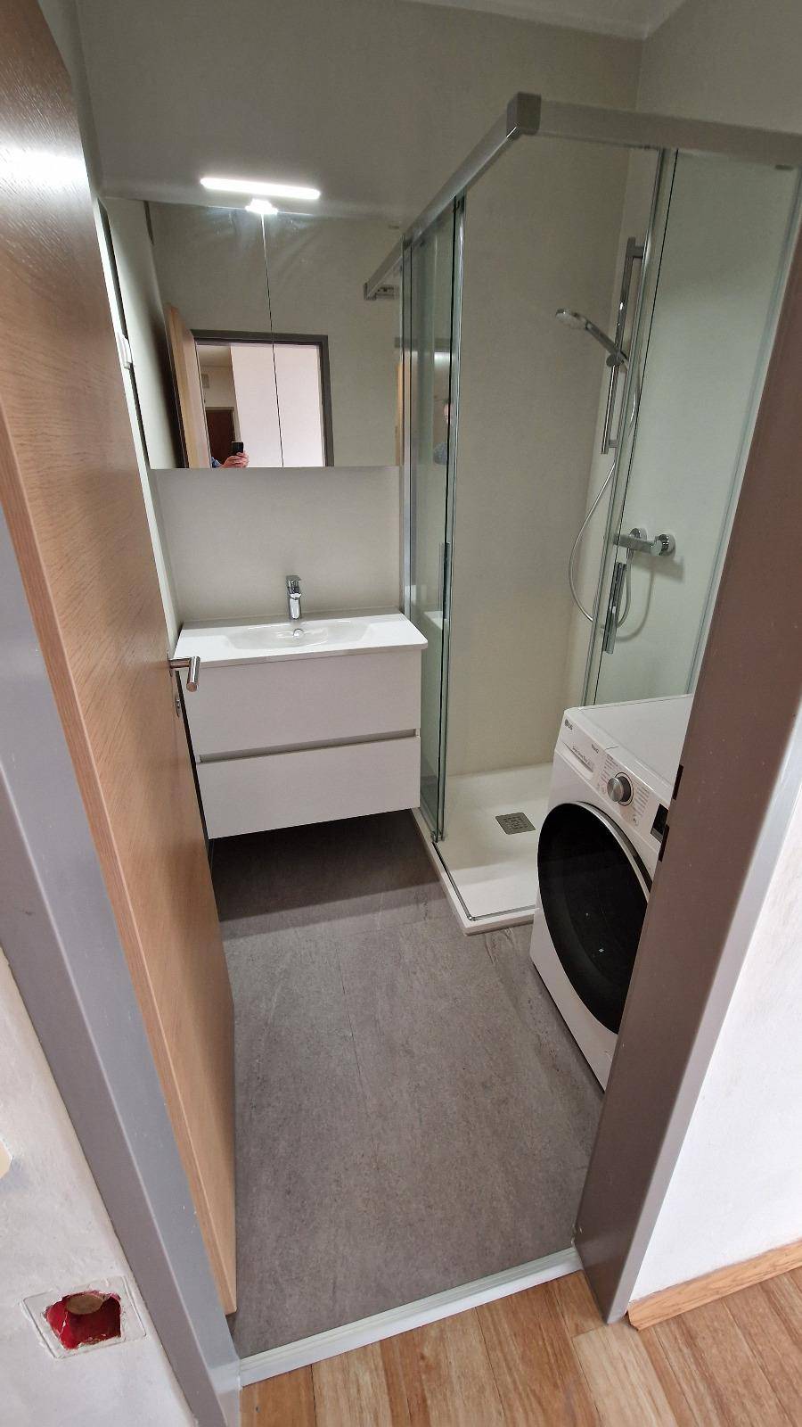 Modernes Badezimmer mit Duschkabine, Waschbeckenunterschrank und integrierter Waschmaschine.