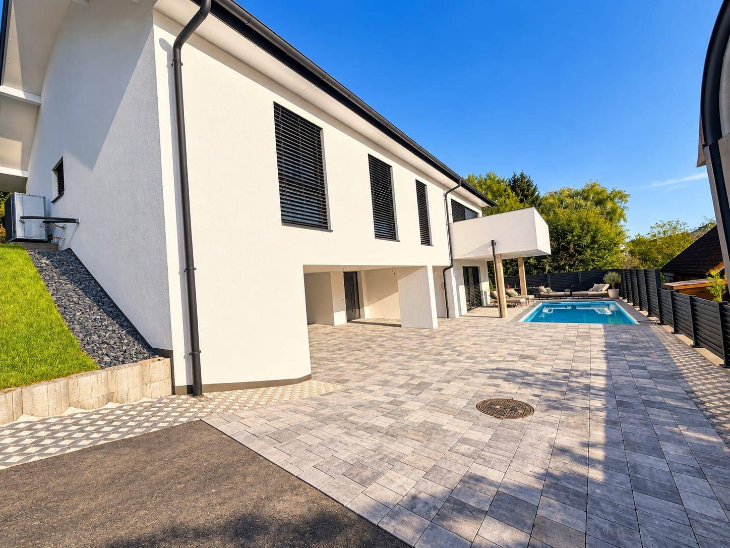 Moderne Architektur des Hauses mit gepflasterter Auffahrt und seitlichem Zugang zum Poolbereich.