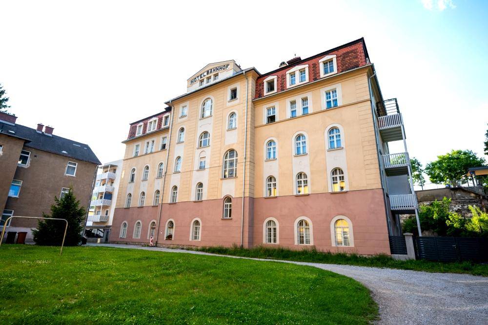 Historisches Hotelgebäude mit gepflegter Rasenfläche und Gehweg unter blauem Himmel.