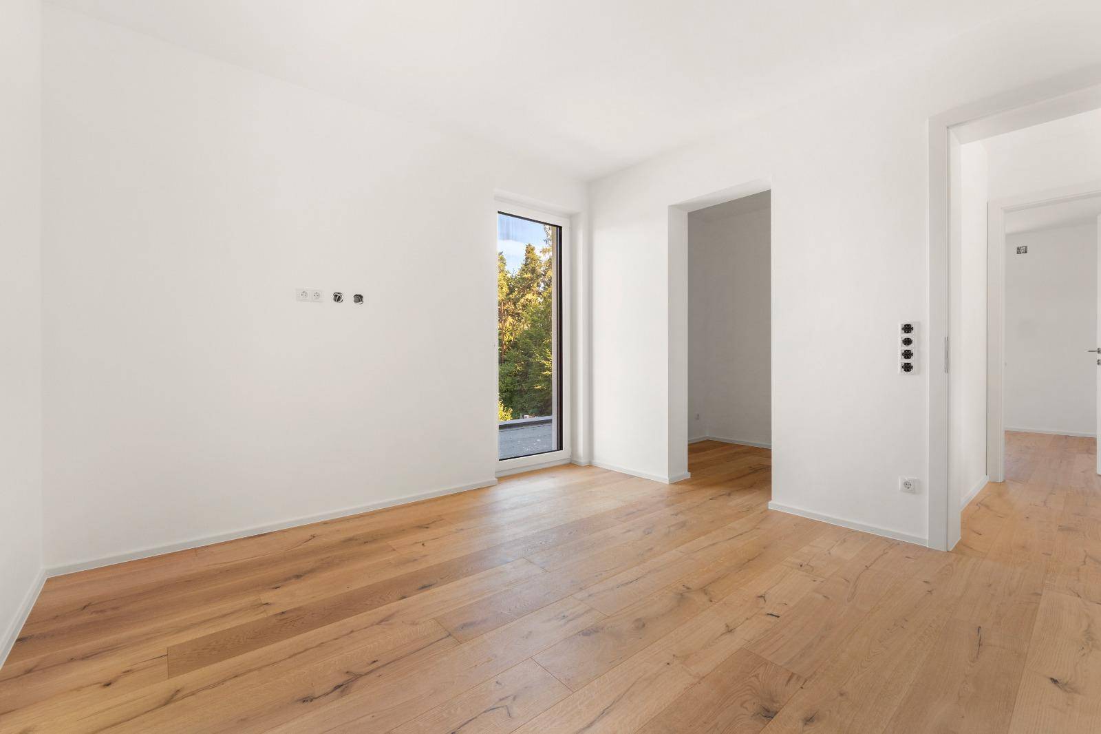 Geräumiges Zimmer mit Eichenparkett und hoher Fenstertür, die viel Licht hereinlässt.
