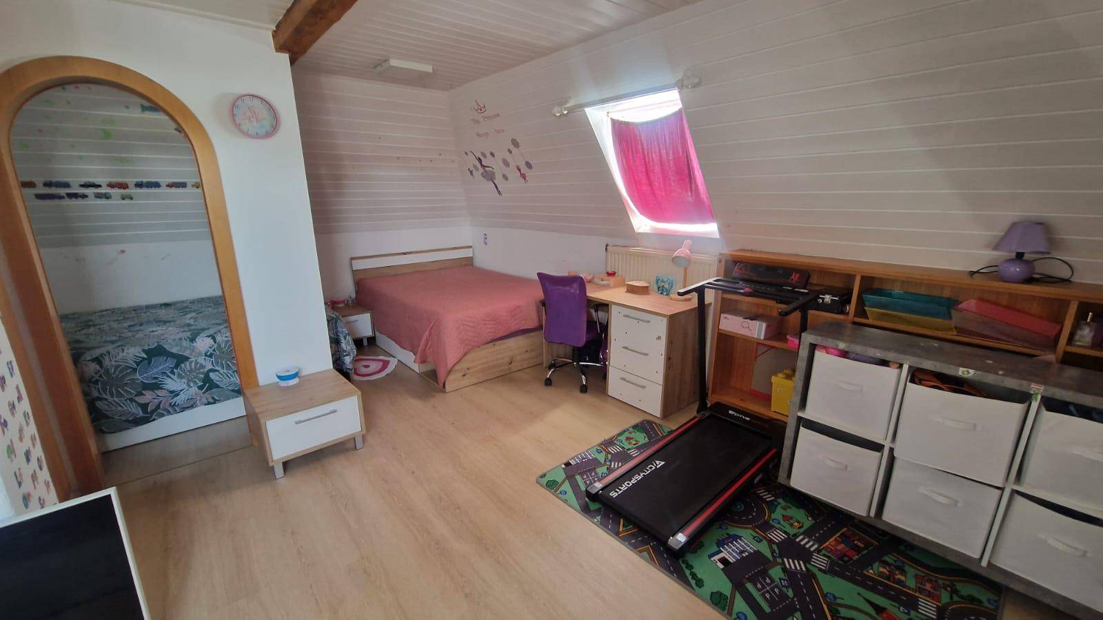 Gemütliches Dachgeschoss-Schlafzimmer mit Bett, Schreibtisch und Zugang zu einem weiteren Schlafbereich.