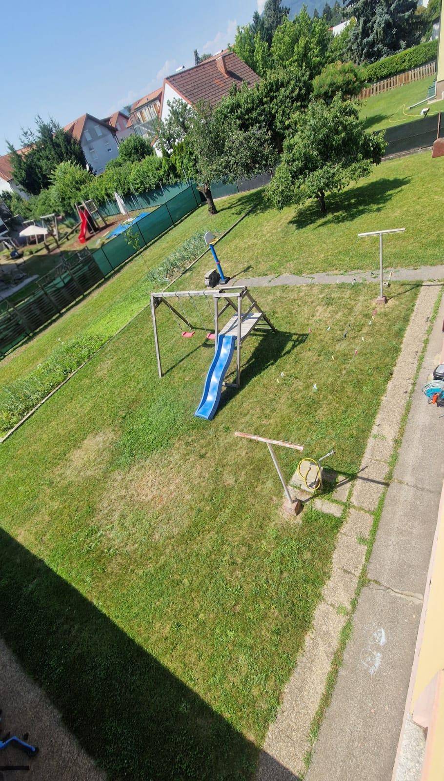 Grüner Gartenbereich mit Kinderspielplatz, Rutsche und Schaukeln, von oben gesehen.