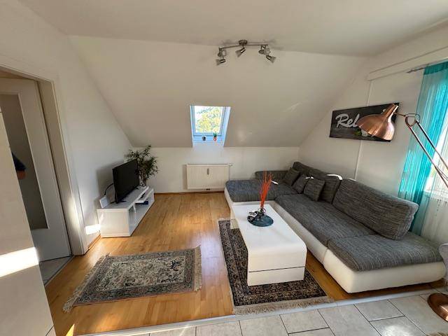 Gemütliches Wohnzimmer im Dachgeschoss mit großem Sofa, Fernseher und Dachfenster.