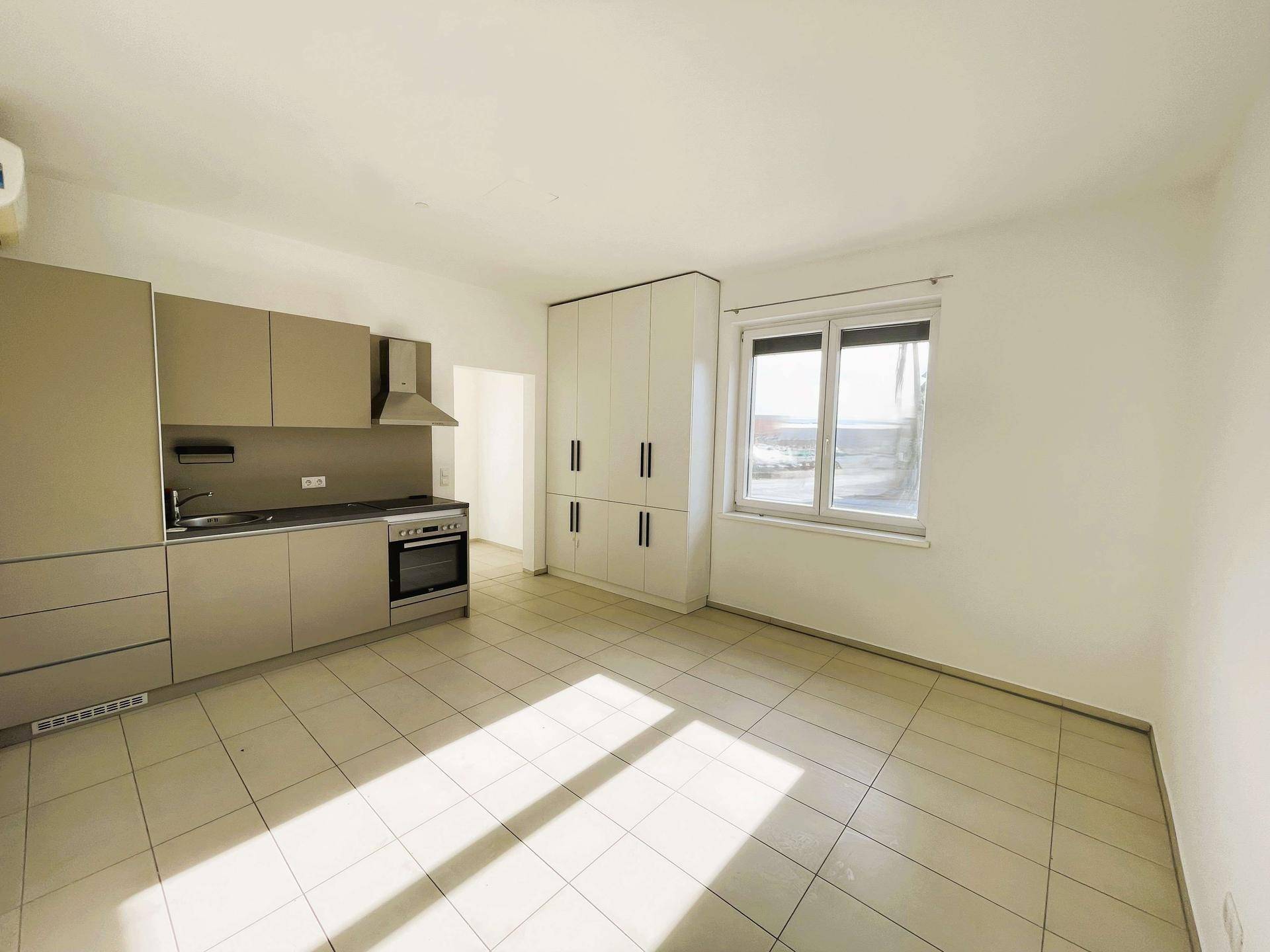 Moderne Einbauküche mit grauen Schränken, Kochfeld und Backofen in hellem Raum.