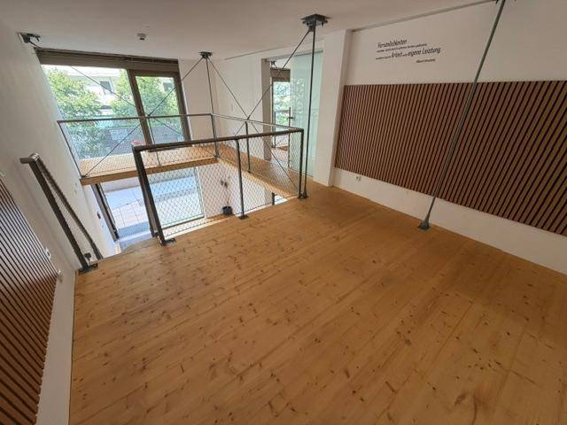 Blick von der Galerie auf den unteren Bereich mit Holzboden, großen Fenstern und dekorativen Wandpaneelen.